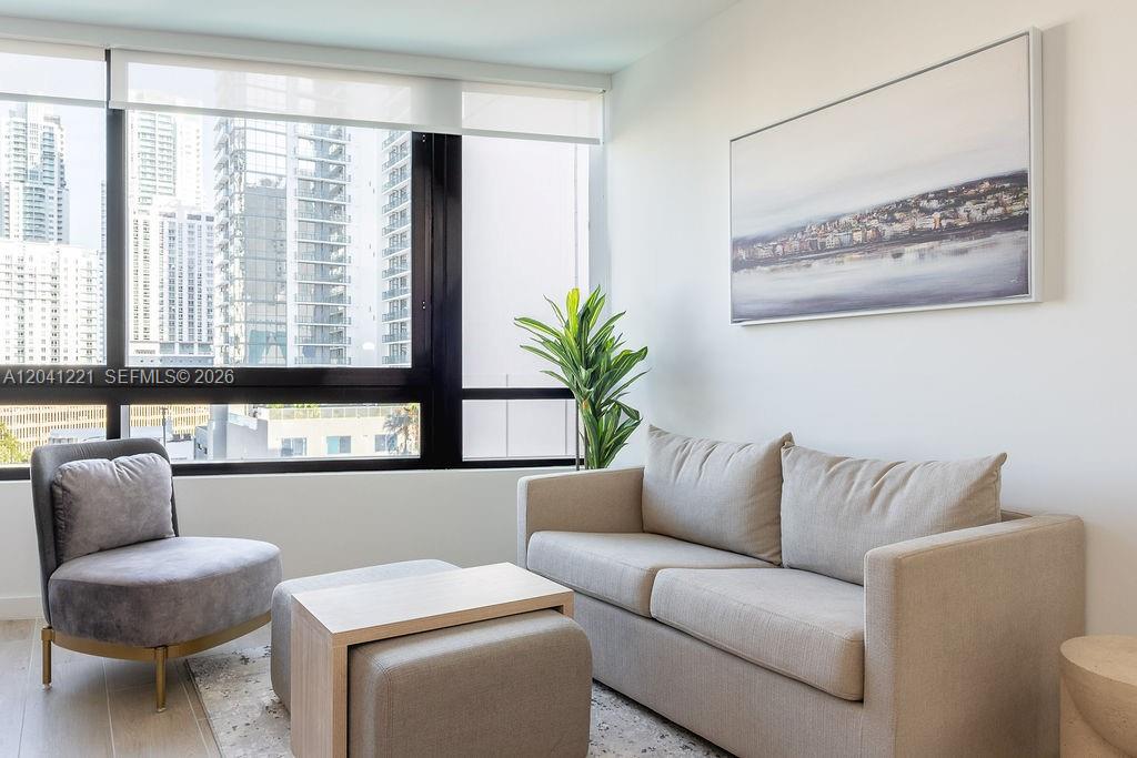 A modern living room features a beige sofa, an armchair, and a city view window — 225 N Miami Ave # 1804, Miami FL 33128, MIAMI, FL