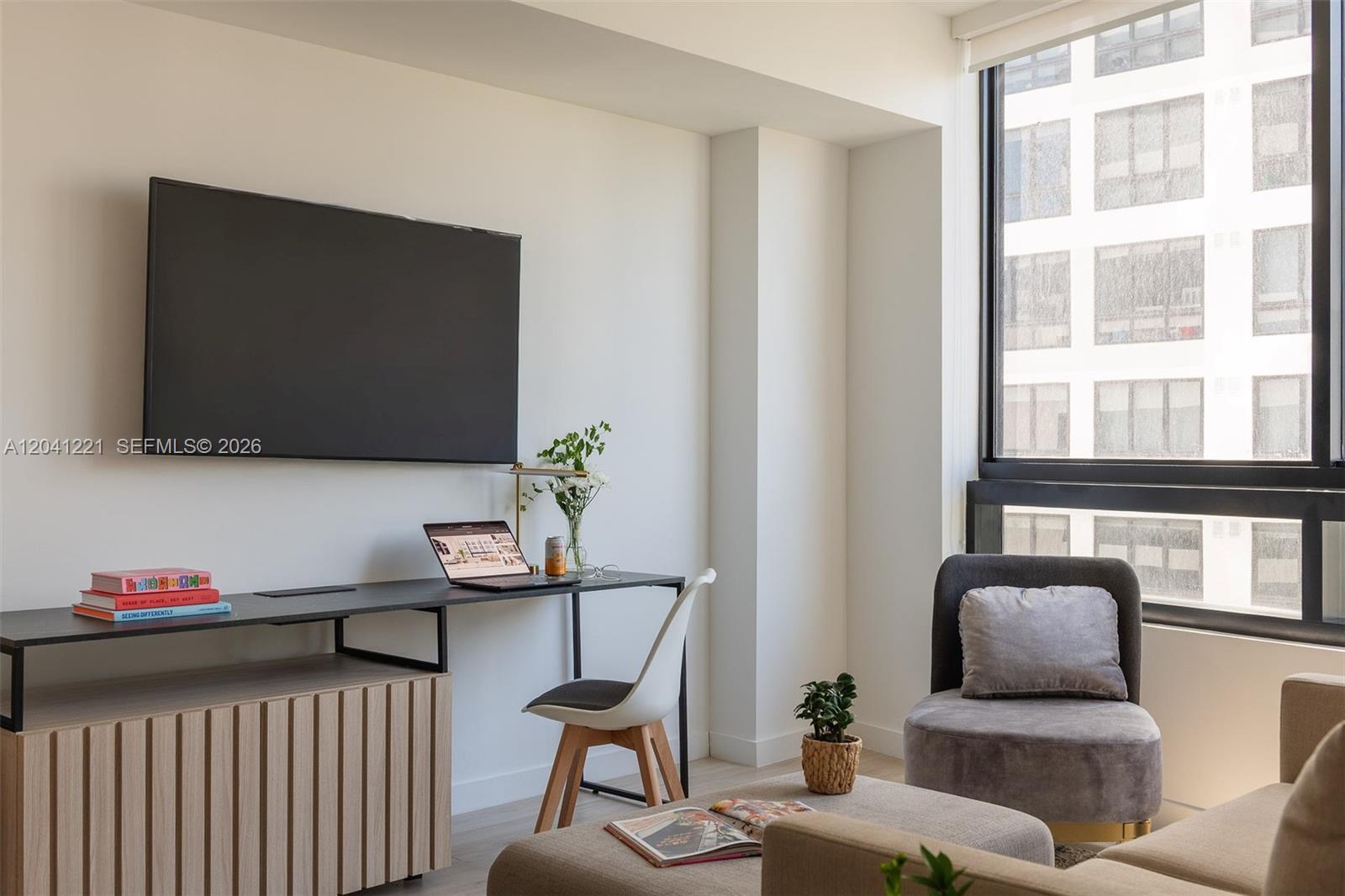 A modern living room features a wall-mounted television, a desk area, and a large window — 225 N Miami Ave # 1804, Miami FL 33128, MIAMI, FL