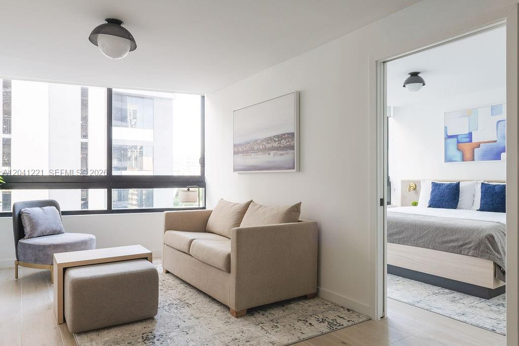 A living room with a beige sofa and armchair leads into a bedroom — 225 N Miami Ave # 1804, Miami FL 33128, MIAMI, FL