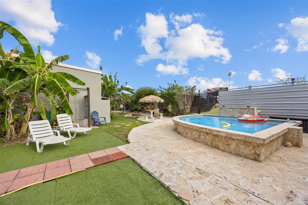 A backyard features a raised stone pool, lounge chairs on artificial turf, and a patio area — Solar 5 CARR 429 BO CALVACHE, RINCON, PR