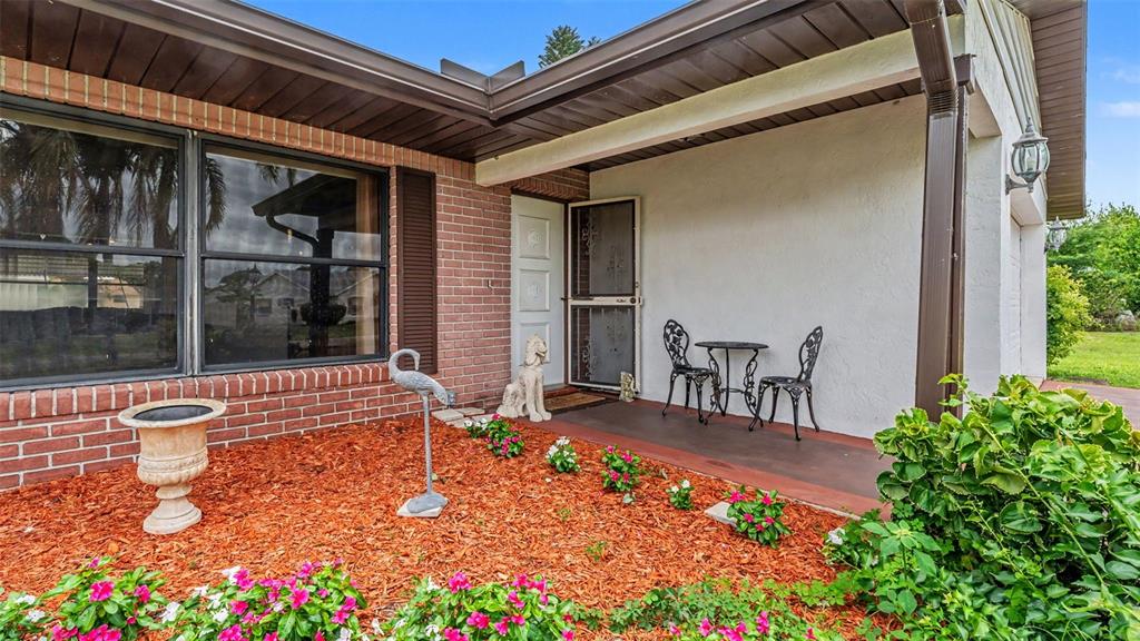 A brick and stucco house exterior features a covered porch with chairs and landscaping — 1711 SUNRISE PLACE, SEBRING, FL