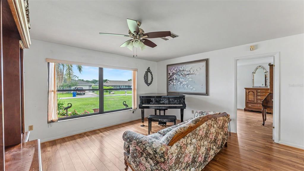 A living room features wood-look flooring, a grand piano, a floral sofa, and a ceiling fan — 1711 SUNRISE PLACE, SEBRING, FL