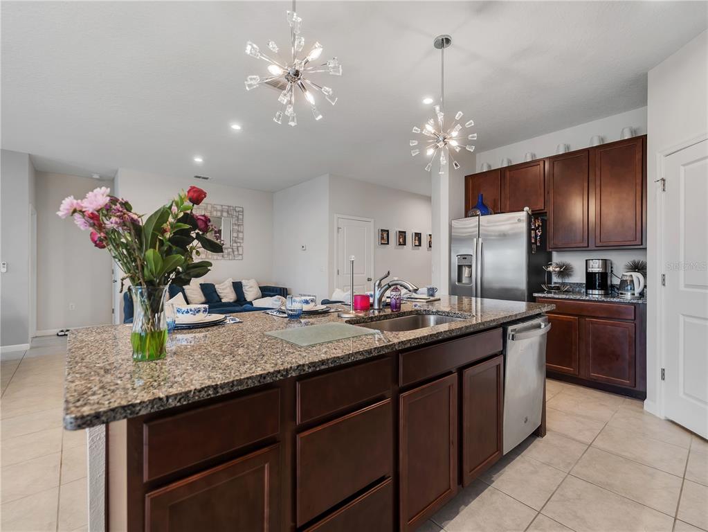A kitchen features a granite-topped island, dark wood cabinetry, stainless steel appliances, and pendant lighting — 5542 TOULOUSE LANE, ST CLOUD, FL