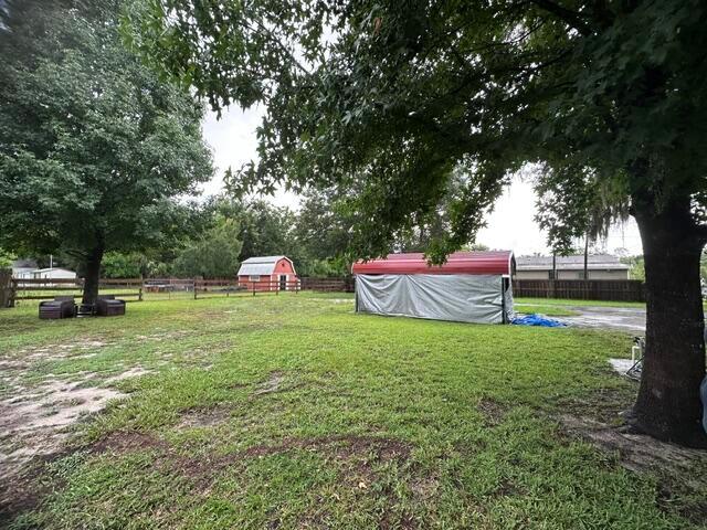 A grassy backyard features a large tree, a red shed, and a covered storage structure — 444 Quail Street, FL 32159, FL
