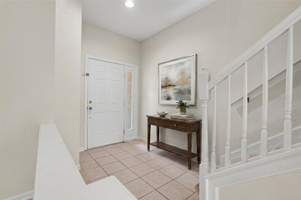 A tiled entryway features a wooden console table, wall art, and a white staircase — 8471 SANDY BEACH STREET, TAMPA, FL