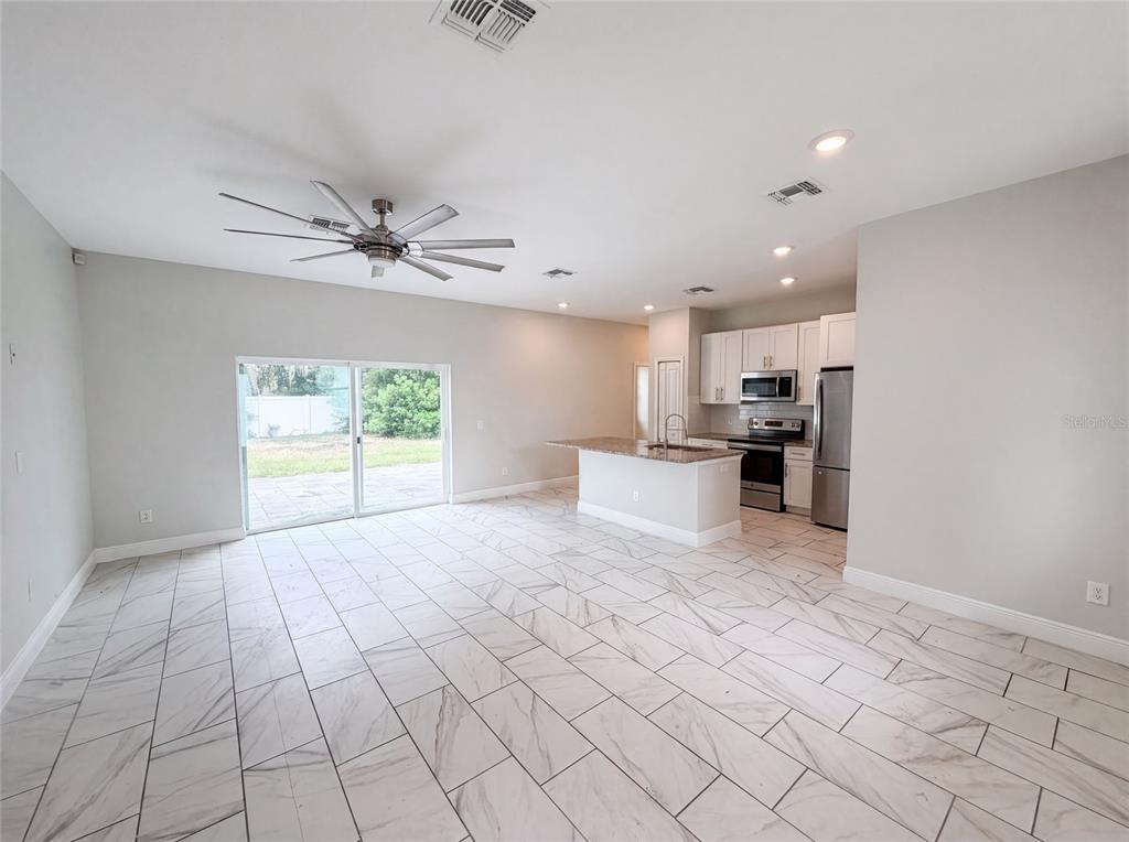 An open-concept kitchen and living area features white tile flooring, a ceiling fan, and sliding doors — 1140 BANCROFT STREET, DELTONA, FL