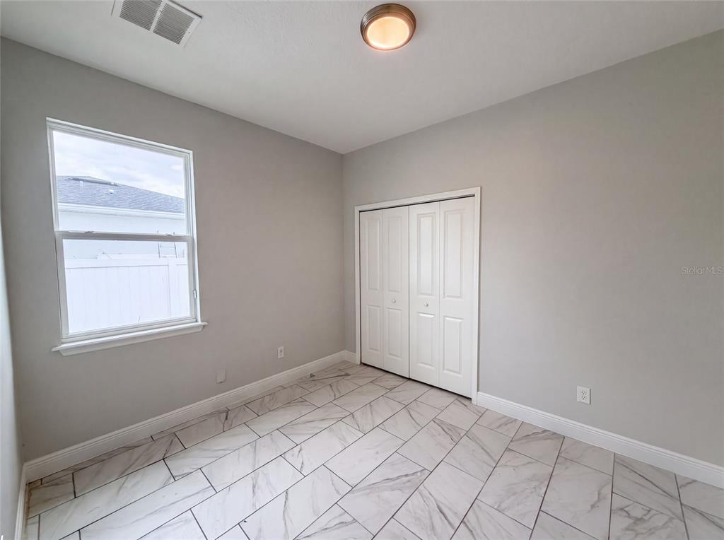 A bedroom with light gray walls, white closet doors, and white marble-look tile flooring — 1140 BANCROFT STREET, DELTONA, FL