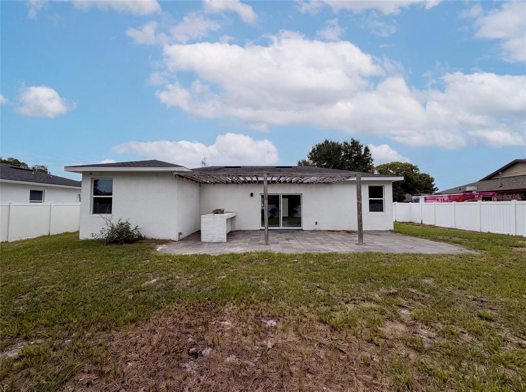 The backyard features a white stucco house with a paved patio and a wooden pergola — 1140 BANCROFT STREET, DELTONA, FL