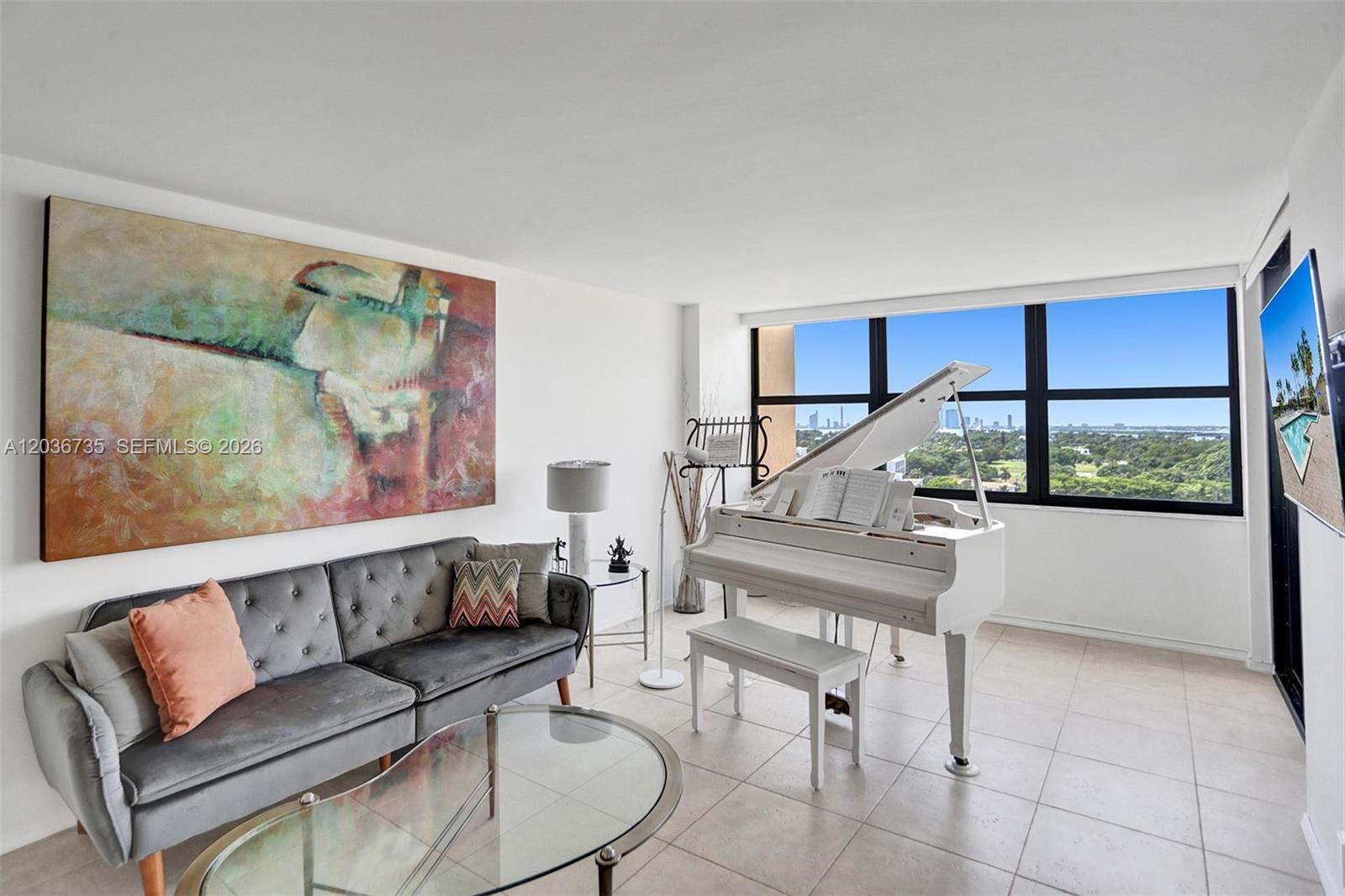 A living room features a grey tufted sofa, a white grand piano, and floor-to-ceiling windows — 2555 Collins Ave # 1508, Miami Beach FL 33140, MIAMI BEACH, FL