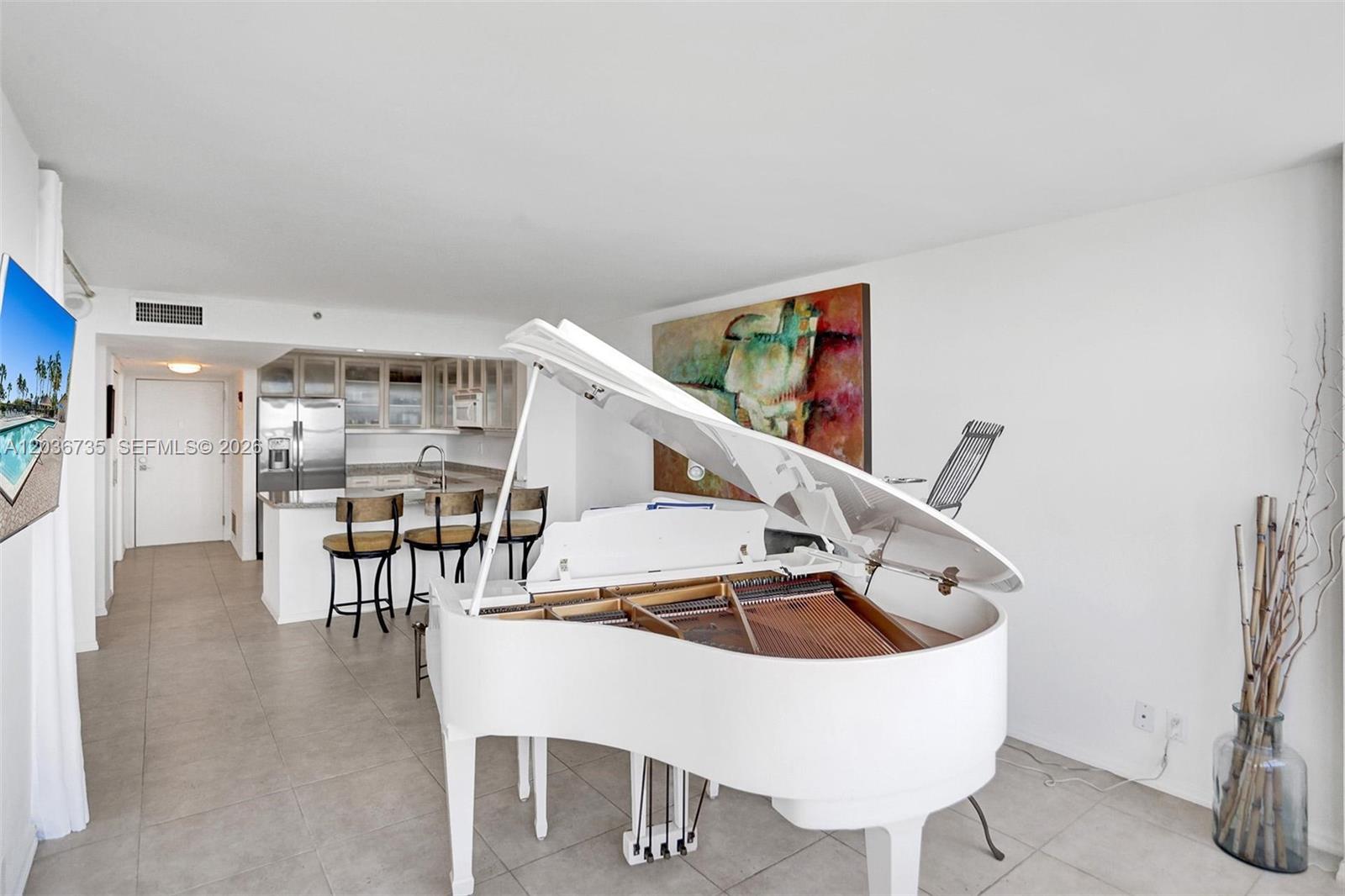 A white grand piano sits in a living area next to an open kitchen — 2555 Collins Ave # 1508, Miami Beach FL 33140, MIAMI BEACH, FL