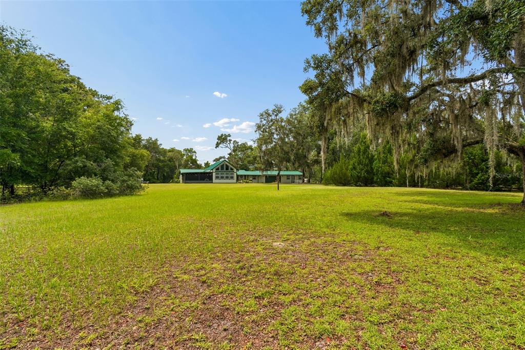 A house with a green roof sits in the distance behind a large grassy field — 11094 SW 51ST DRIVE, WEBSTER, FL