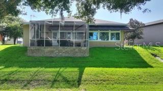 A tan house with a screened-in patio and a stone retaining wall sits on a lawn — 492 MEANDERING WAY, POLK CITY, FL