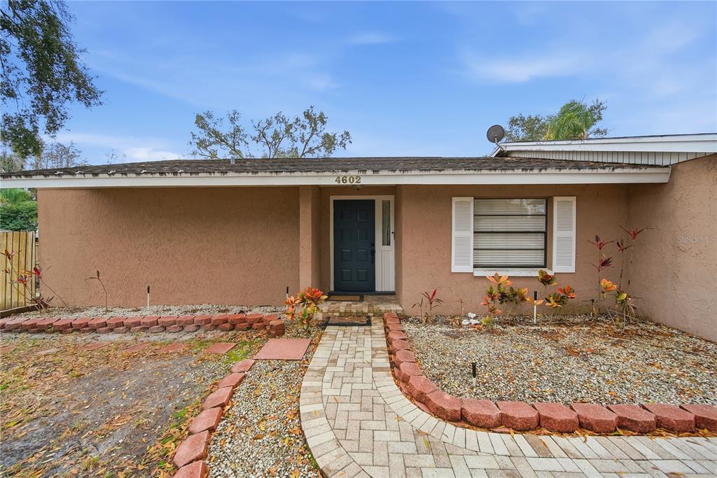 A single-story house with a tan stucco exterior, a dark front door, and a brick walkway — 4602 BUCKEYE ROAD, TAMPA, FL