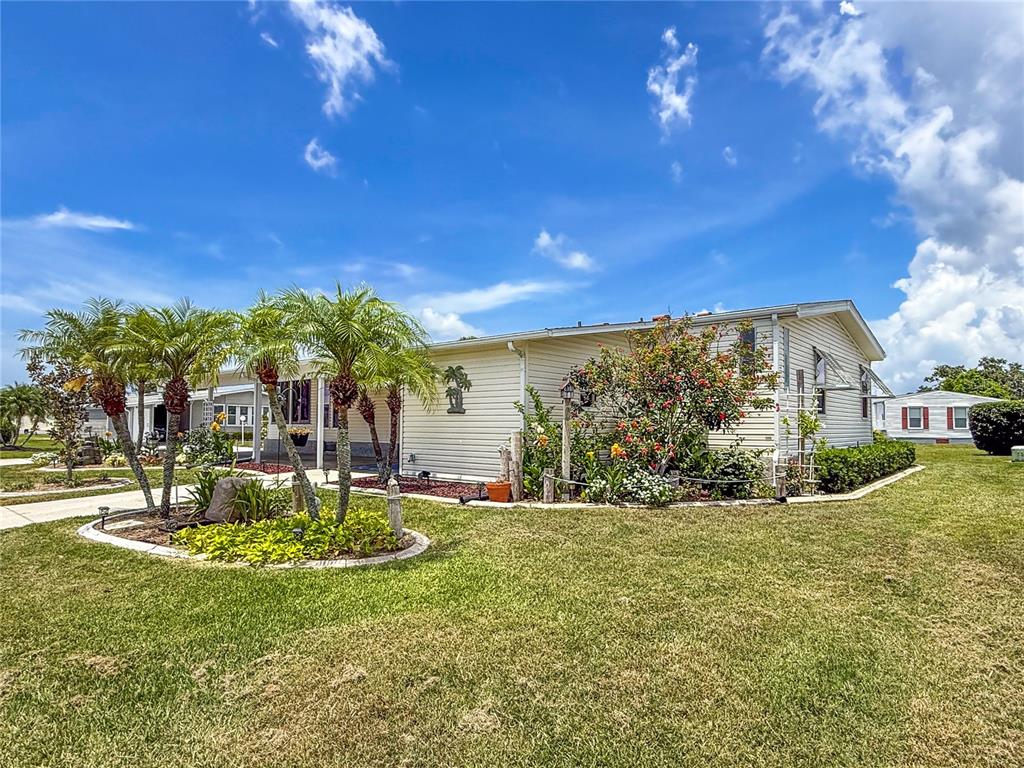 A light-colored mobile home with palm trees and landscaping sits on a grassy lot — 73 WHIPPORWILL COURT, ELLENTON, FL