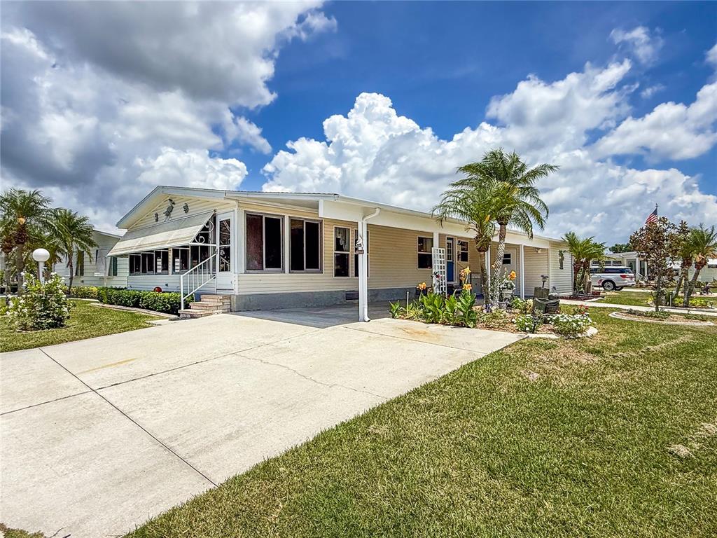A single-story manufactured home with a concrete driveway, palm trees, and a covered front porch — 73 WHIPPORWILL COURT, ELLENTON, FL