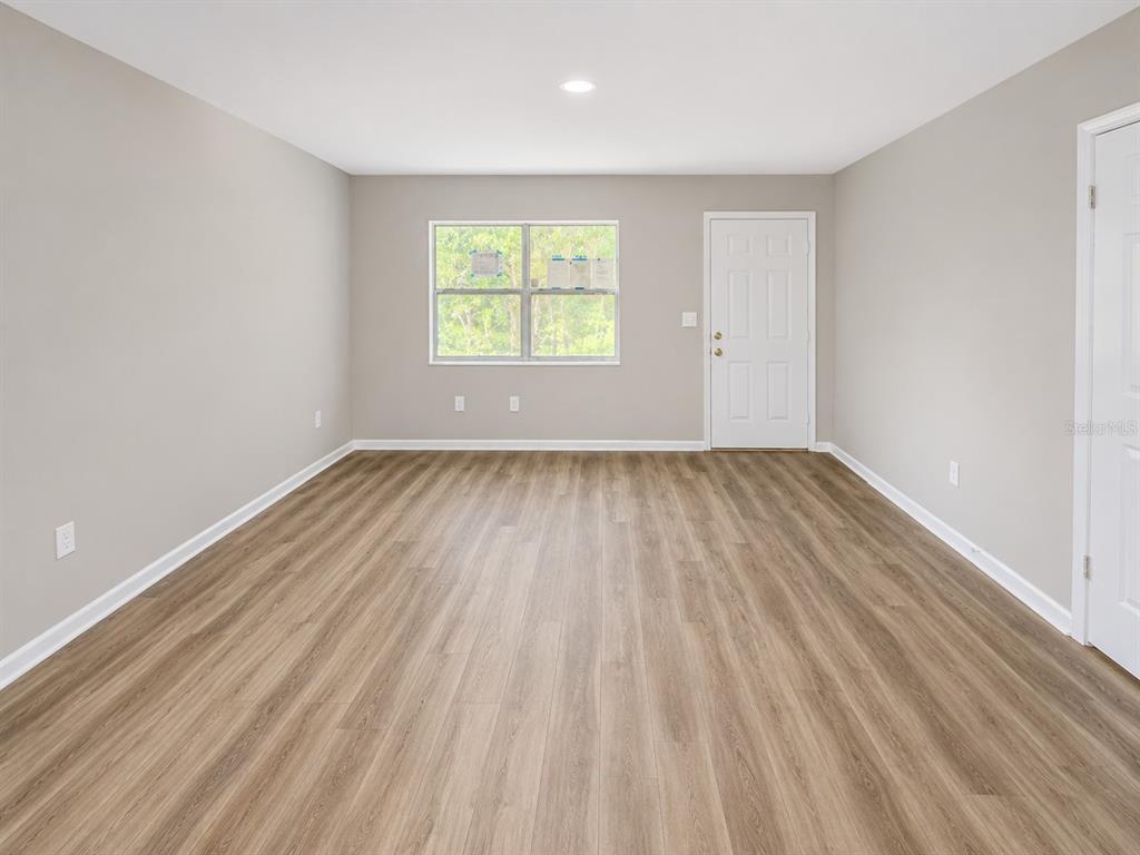 An empty room with light gray walls, wood-look flooring, a window, and a white door — 21450 NE 35TH STREET, WILLISTON, FL
