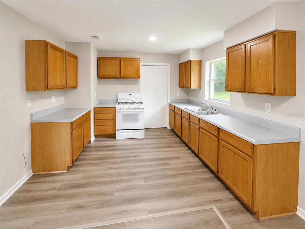 A kitchen with oak cabinets, light gray countertops, white appliances, and wood-look vinyl flooring — 21450 NE 35TH STREET, WILLISTON, FL