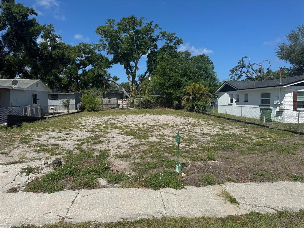 A vacant, sandy residential lot is situated between two small houses under a blue sky — 6803 S CORTEZ STREET, TAMPA, FL