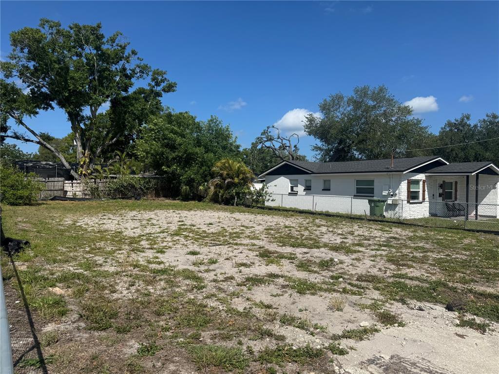 A vacant, sandy lot sits next to a white single-story house with a black roof — 6803 S CORTEZ STREET, TAMPA, FL