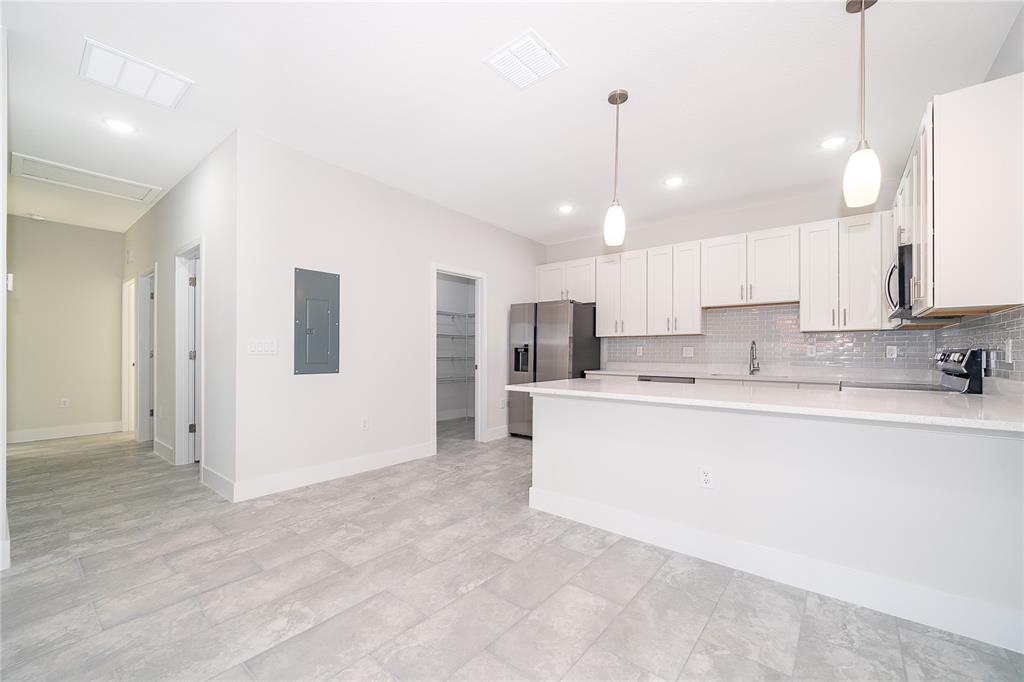 A modern kitchen features white cabinetry, stainless steel appliances, quartz countertops, and gray tile flooring — 1661 CUMIN DRIVE, KISSIMMEE, FL