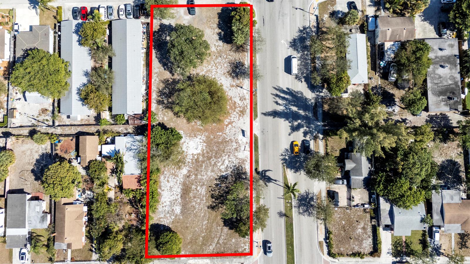 This aerial view shows an empty rectangular lot outlined in red next to a road — 1212 10th Avenue N, FL 33460, FL