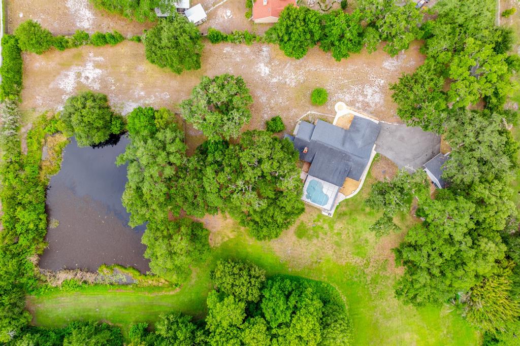 An aerial view shows a house with a pool, a pond, and surrounding trees — 1600 E 10TH STREET, ST CLOUD, FL