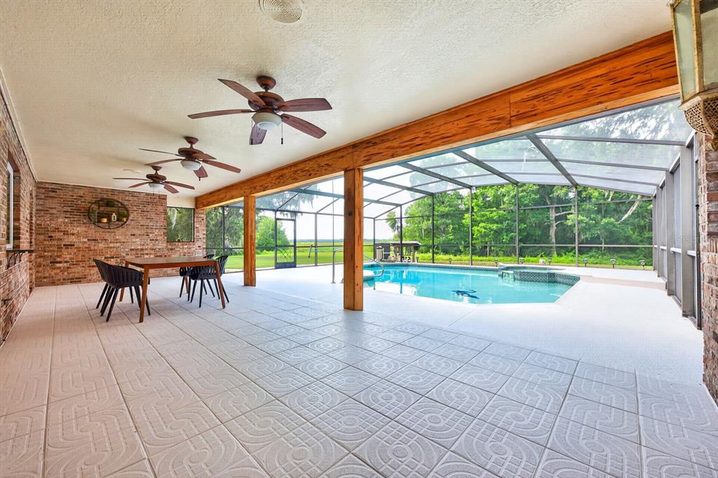 A covered patio with brick walls, ceiling fans, and a screened-in pool overlooking a field — 1600 E 10TH STREET, ST CLOUD, FL