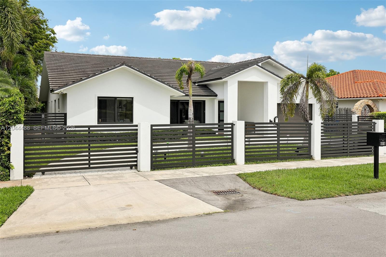 A white single-story house features a dark tiled roof and a horizontal slat metal fence — 6816 SW 89th Ct, Miami FL 33173, MIAMI, FL