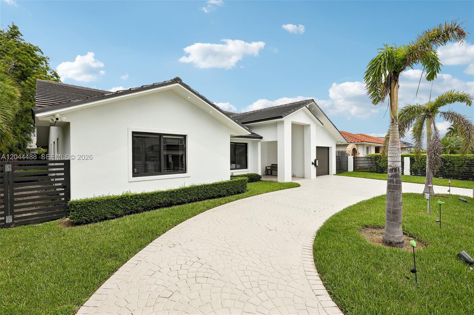 A white single-story house features a curved paver driveway, a palm tree, and black fencing — 6816 SW 89th Ct, Miami FL 33173, MIAMI, FL