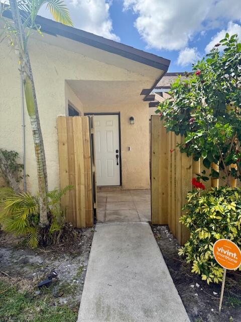 A concrete walkway leads to a white front door framed by wooden privacy fences — 1803 Waterview Circle, Palm Springs FL 33461, PALM SPRINGS, FL