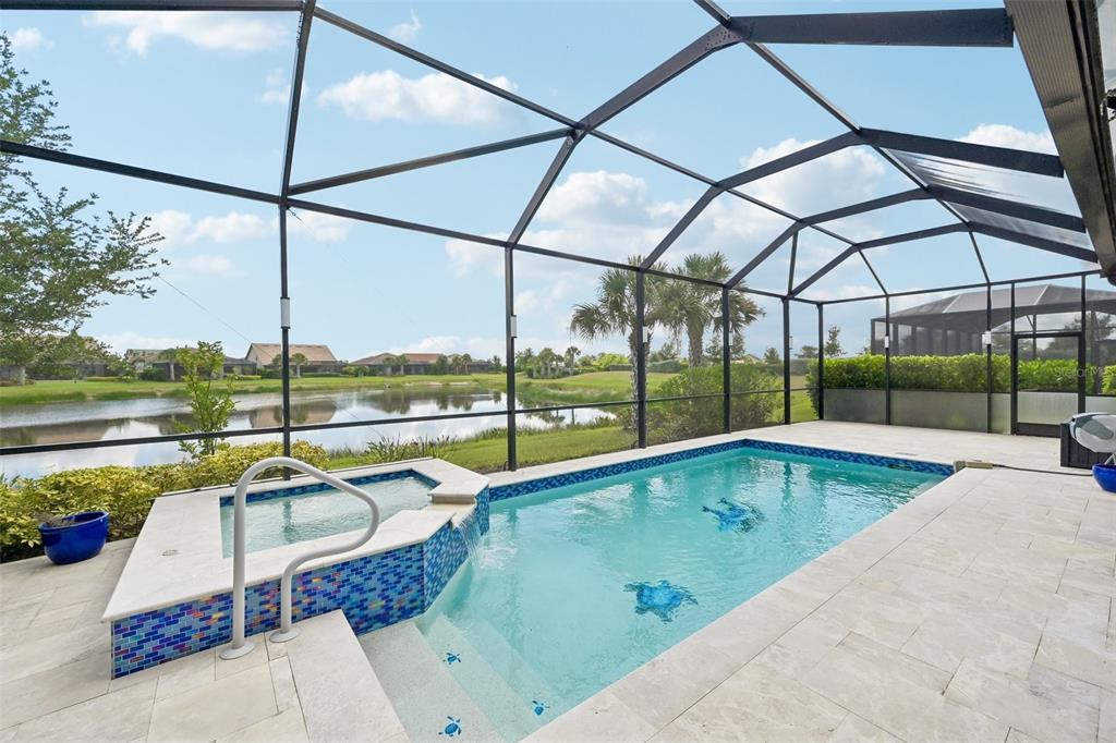 A screened-in pool and spa area with light stone decking overlooking a pond — 13356 VERANDI STREET, VENICE, FL
