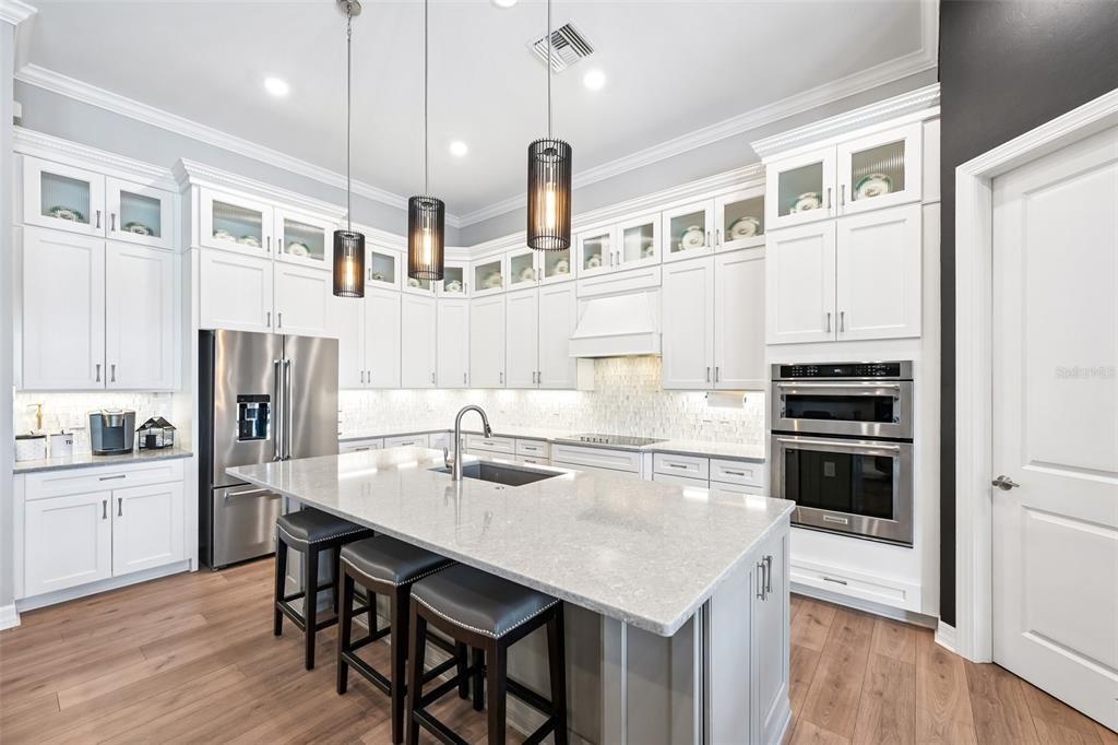 A modern kitchen features white cabinetry, a gray island with bar stools, and stainless appliances — 13356 VERANDI STREET, VENICE, FL