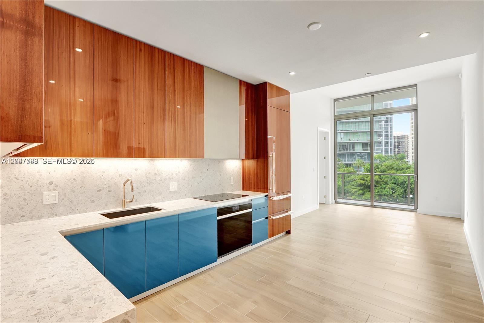 A modern kitchen features blue lower cabinets, wood-toned upper cabinets, and a balcony view — 2655 S Bayshore Dr # 403, Miami FL 33133, MIAMI, FL