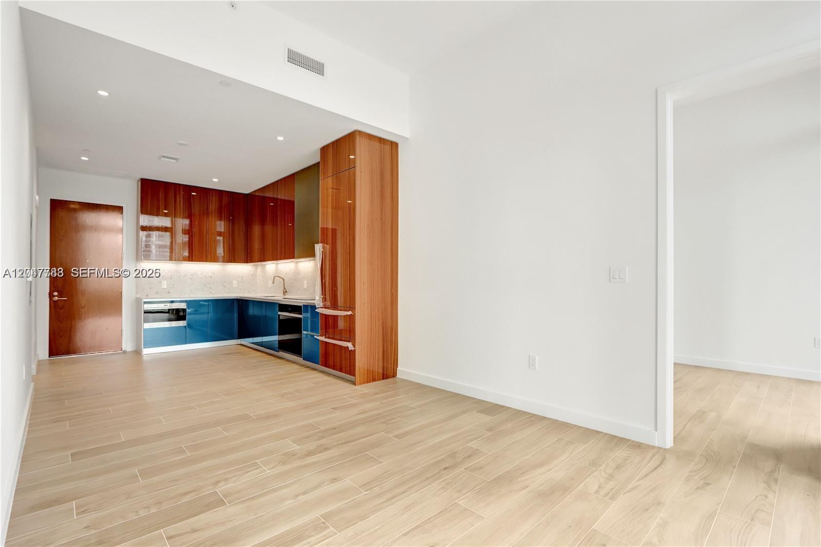 A modern kitchen features blue lower cabinets, wood-toned upper cabinets, and light wood-look flooring — 2655 S Bayshore Dr # 403, Miami FL 33133, MIAMI, FL