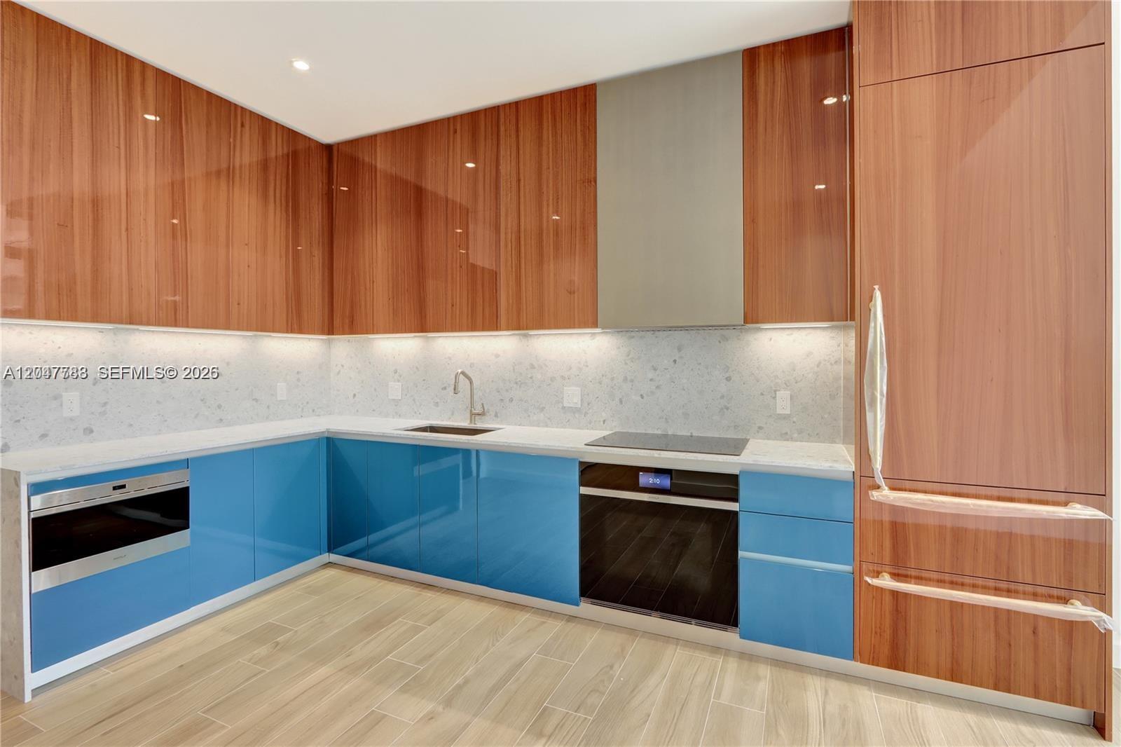A modern kitchen features blue lower cabinets, wood-grain upper cabinets, and a light stone countertop — 2655 S Bayshore Dr # 403, Miami FL 33133, MIAMI, FL