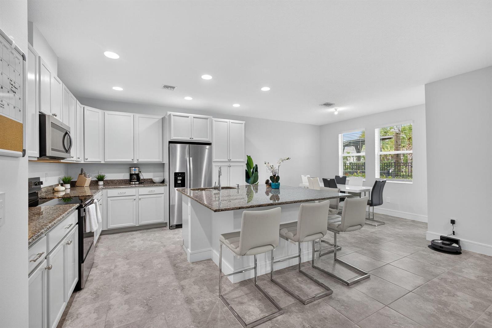 A kitchen features white cabinets, granite countertops, a central island with bar seating, and tile flooring — 16131 Oakview Drive, Westlake FL 33470, WESTLAKE, FL