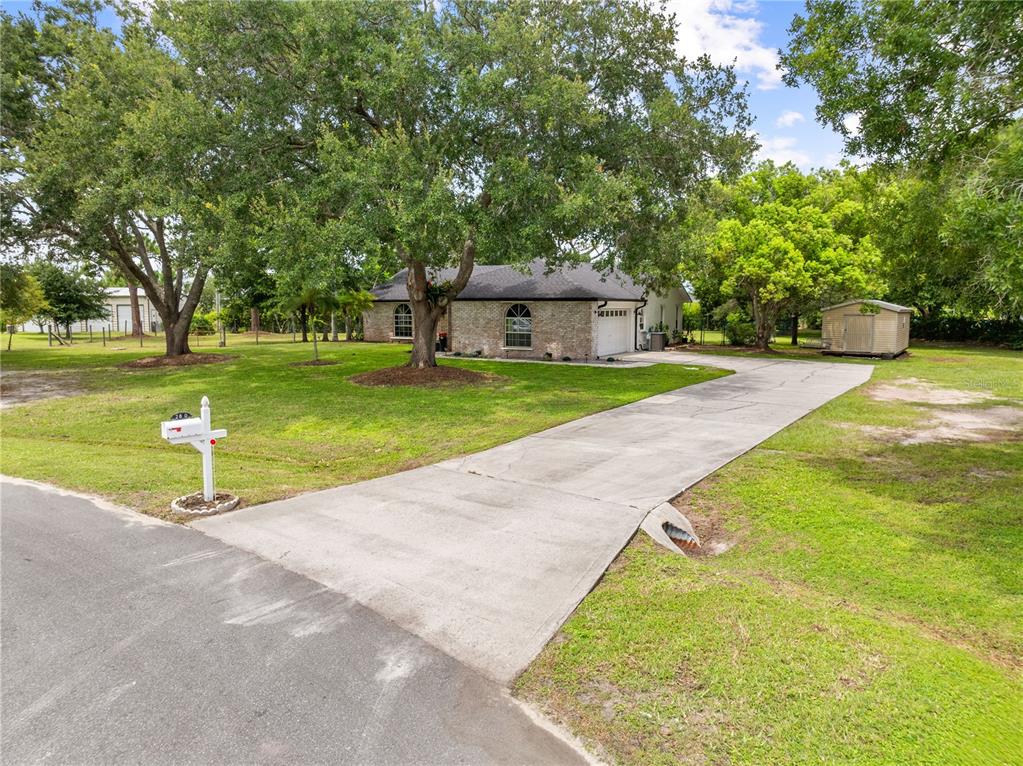 A brick house with a concrete driveway, a mailbox, and a shed on a grassy lot — 2810 WINDSONG LANE, ST CLOUD, FL