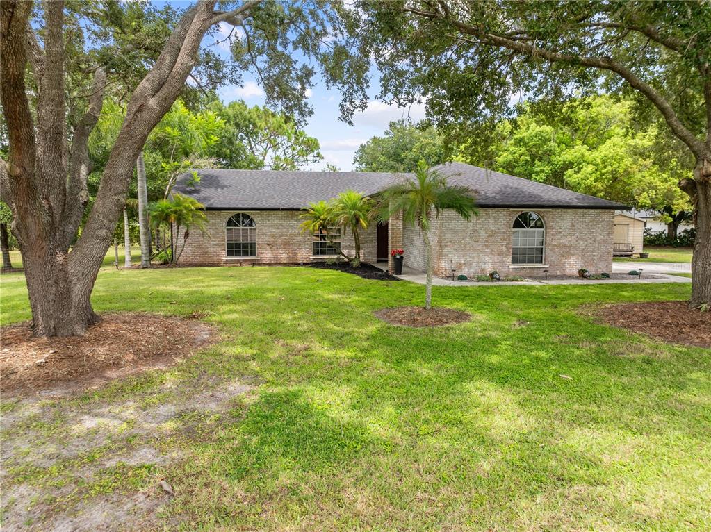 A single-story brick house with a dark shingled roof sits on a grassy, tree-shaded lot — 2810 WINDSONG LANE, ST CLOUD, FL