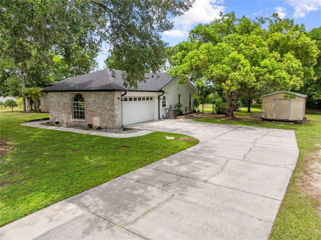 A brick-sided house with a garage, concrete driveway, and a detached shed in the yard — 2810 WINDSONG LANE, ST CLOUD, FL