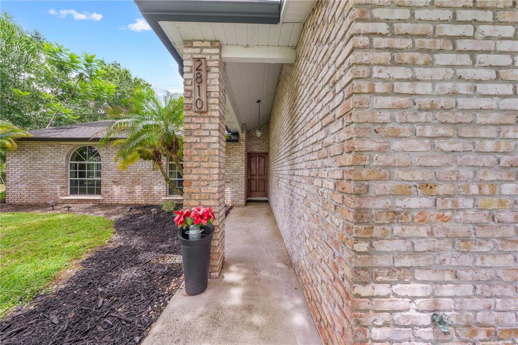 A brick house exterior features a covered entryway, a front door, and a potted plant — 2810 WINDSONG LANE, ST CLOUD, FL