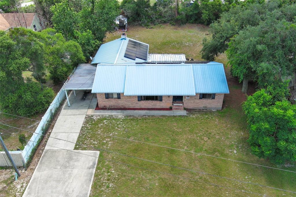 An aerial view shows a brick house with a blue metal roof and solar panels — 2788 BENROCK TERRACE, DELTONA, FL