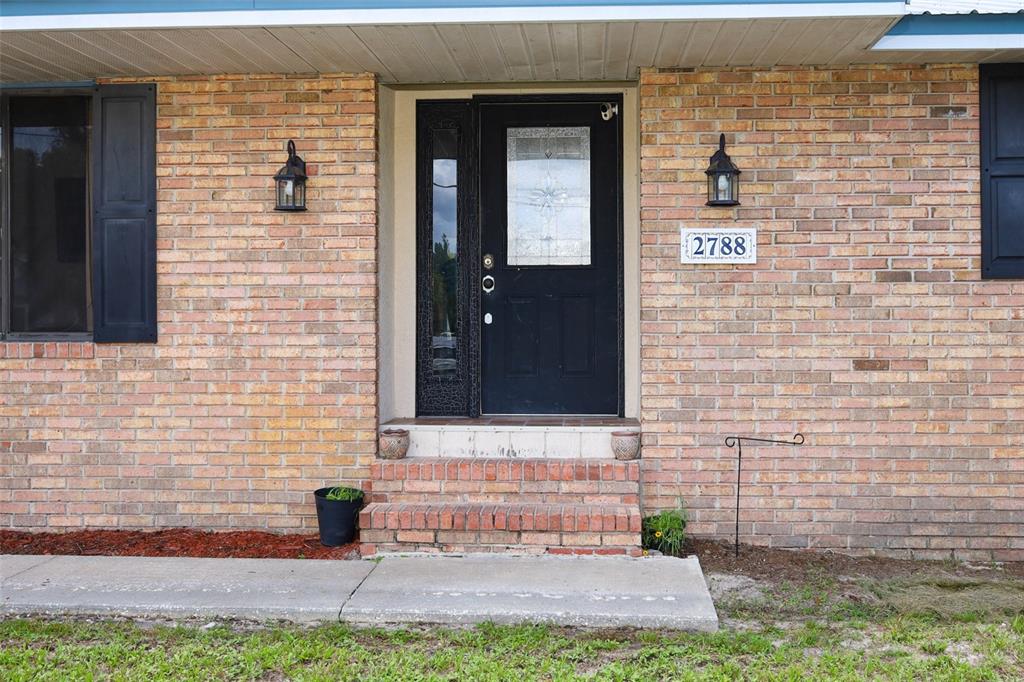 A brick house exterior features a black front door with a sidelight and two lanterns — 2788 BENROCK TERRACE, DELTONA, FL