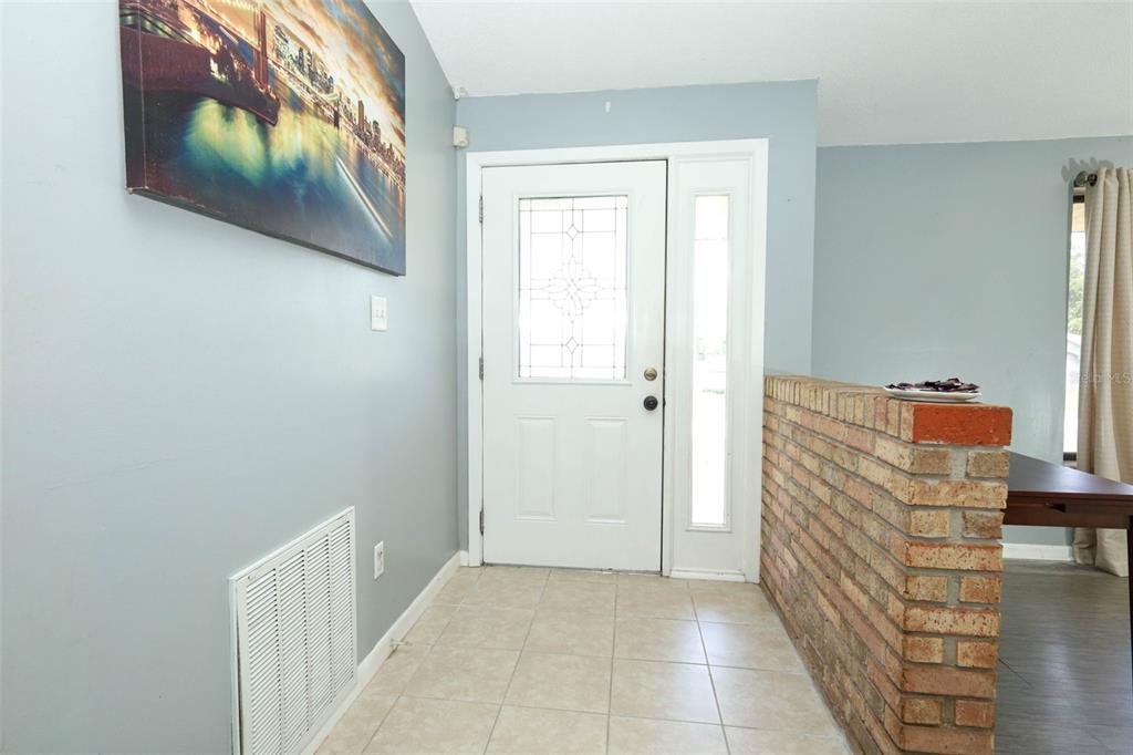 An entryway features light blue walls, a white front door, and a brick half-wall divider — 2788 BENROCK TERRACE, DELTONA, FL
