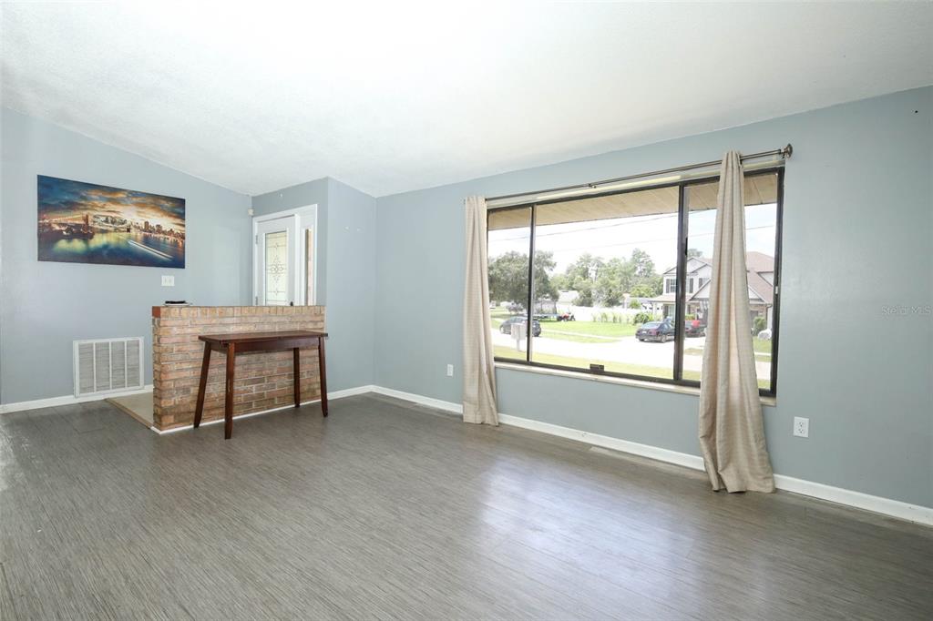 A living room with gray walls, wood-look flooring, a brick half-wall, and a large window — 2788 BENROCK TERRACE, DELTONA, FL