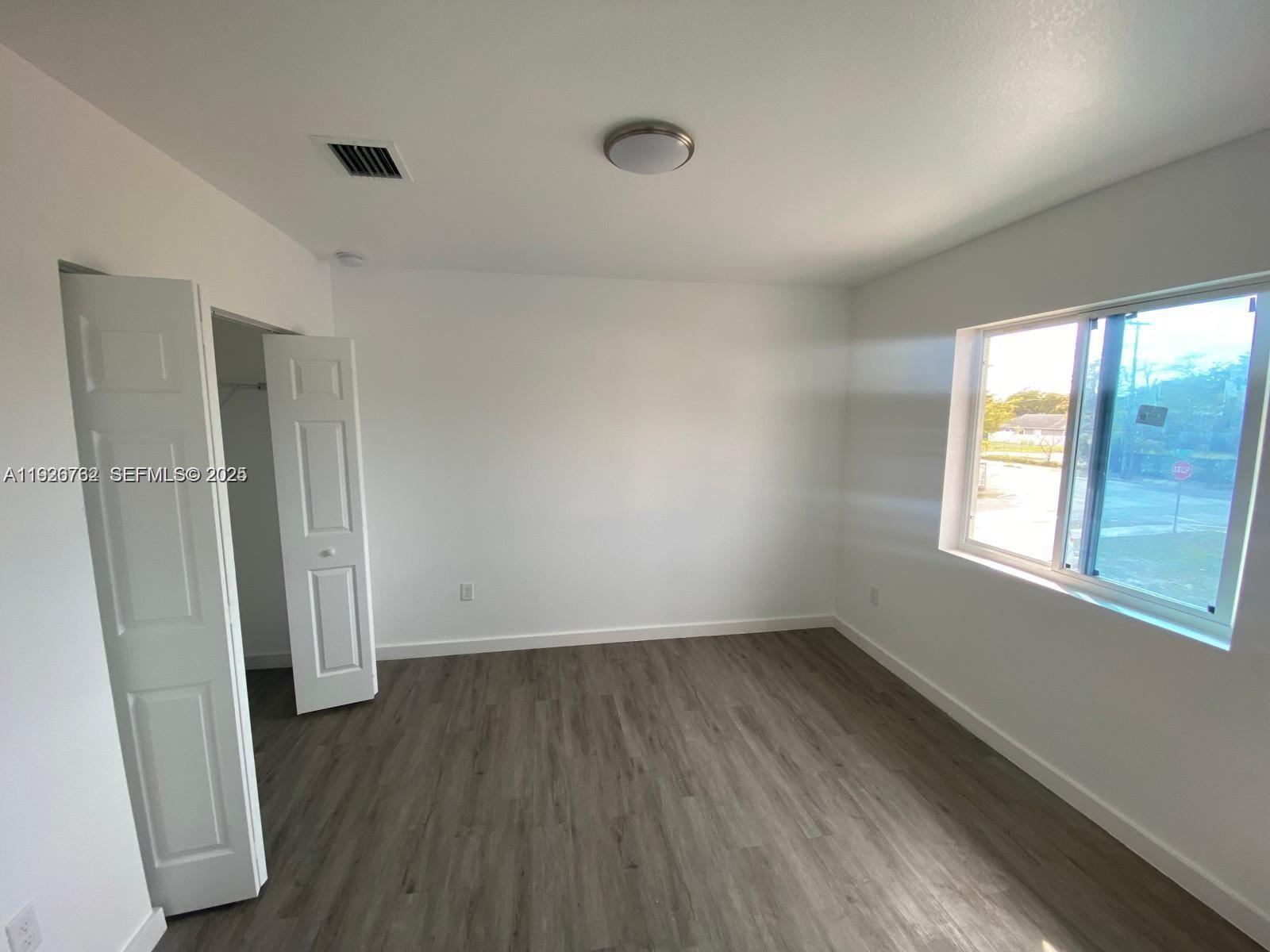 An empty bedroom features white walls, gray wood-look flooring, a closet, and a window — 1783 NW 65th St # 1783, Miami FL 33147, MIAMI, FL