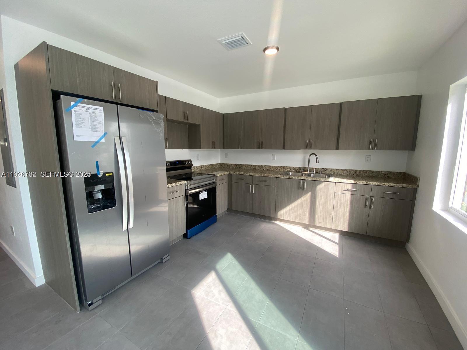 A kitchen features gray wood-grain cabinets, stainless steel appliances, granite countertops, and gray tile flooring — 1783 NW 65th St # 1783, Miami FL 33147, MIAMI, FL