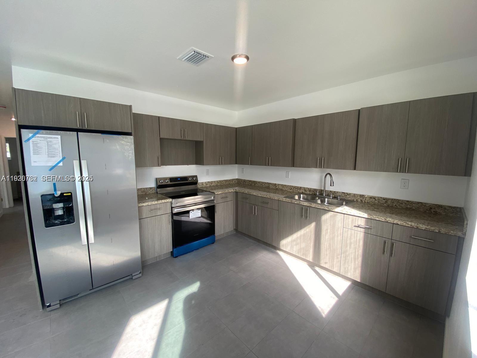 A kitchen features gray wood-grain cabinets, granite countertops, stainless steel appliances, and gray tile flooring — 1783 NW 65th St # 1783, Miami FL 33147, MIAMI, FL