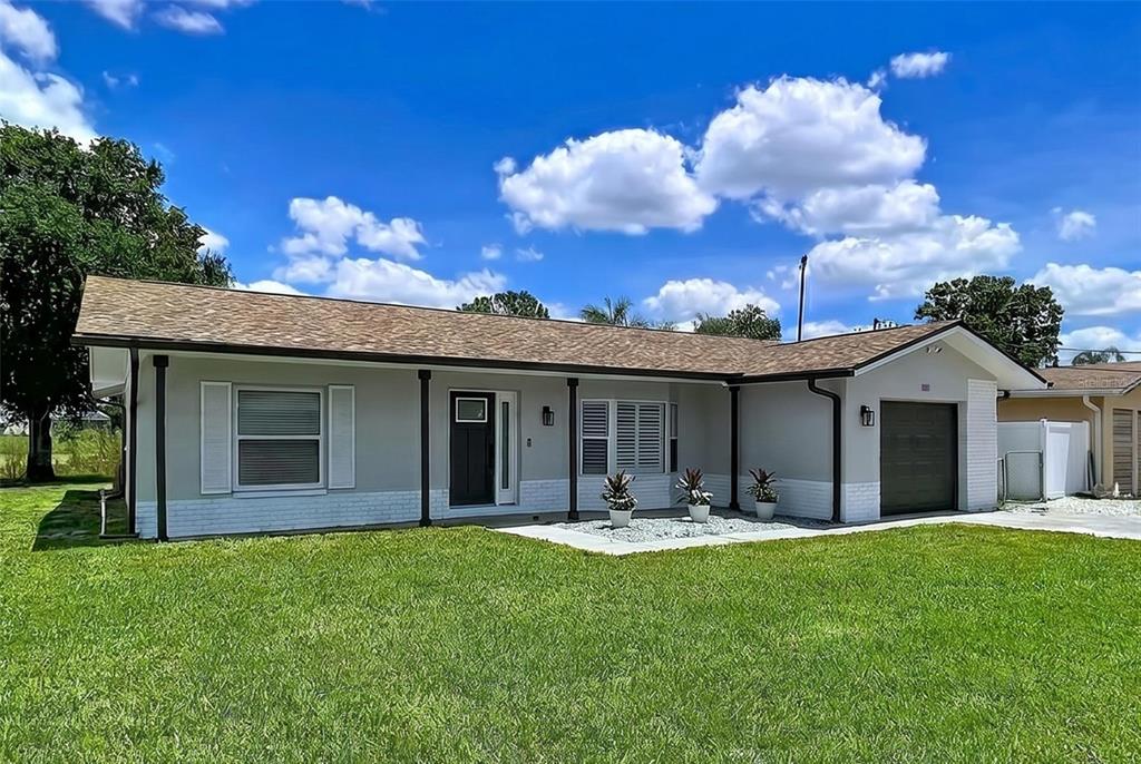 A single-story house with a gray exterior, white brick base, and a dark garage door — 381 WESTWINDS DRIVE, PALM HARBOR, FL