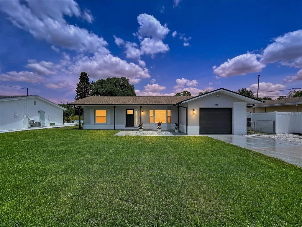 A single-story house with a gray exterior, a dark garage door, and a large lawn — 381 WESTWINDS DRIVE, PALM HARBOR, FL
