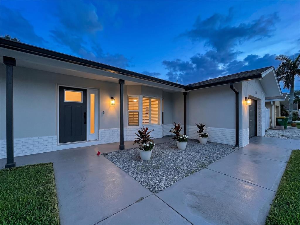 The exterior of a single-story house features a gray facade, white brick accents, and a gravel garden — 381 WESTWINDS DRIVE, PALM HARBOR, FL